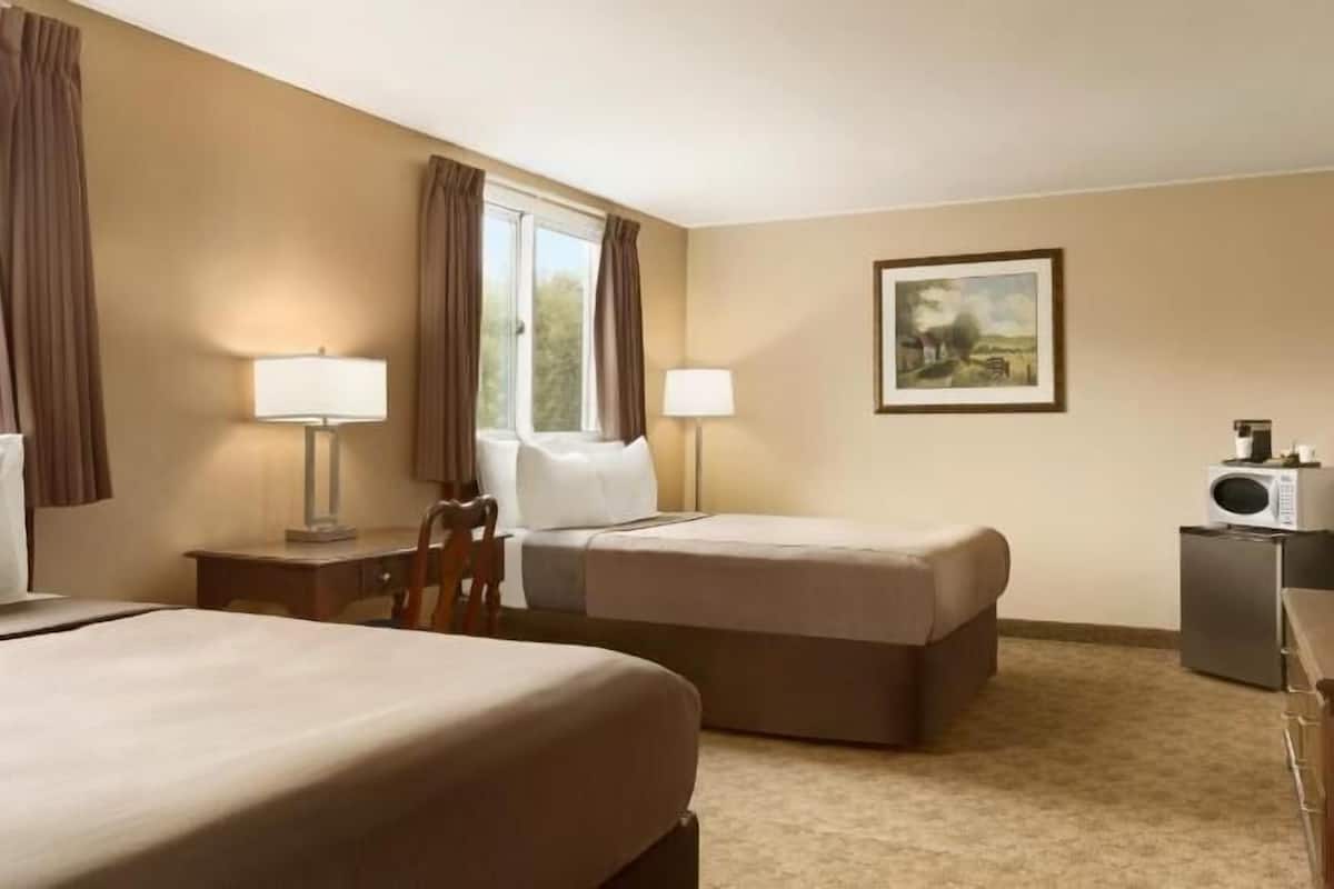 A hotel room with two beds, a desk, two lamps, a television, and a painting on the wall.