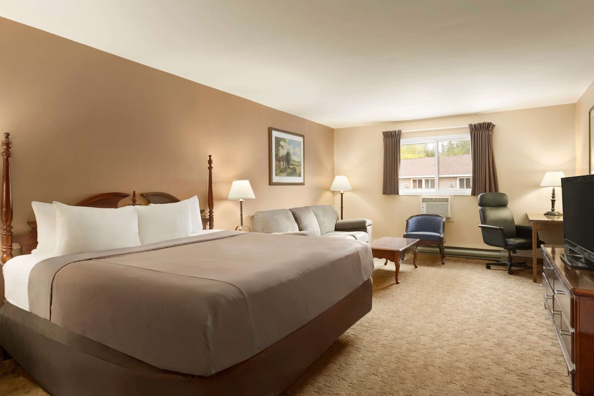 A hotel room with a large bed, two chairs, a desk, a television, and a window with curtains.