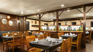 Un restaurante con cabinas y mesas de madera, un salpicadero de azulejos con un reloj, y techo de madera.