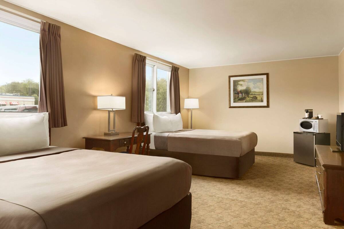 A hotel room with two beds, a desk, a chair, a TV, and a microwave.