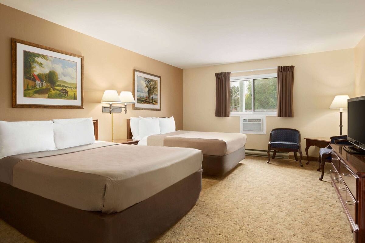 A hotel room with two beds, a desk, a chair, a television, and two paintings on the wall.