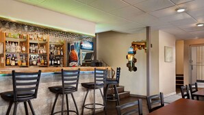 Zona de bar con barra, taburetes y una variedad de botellas.