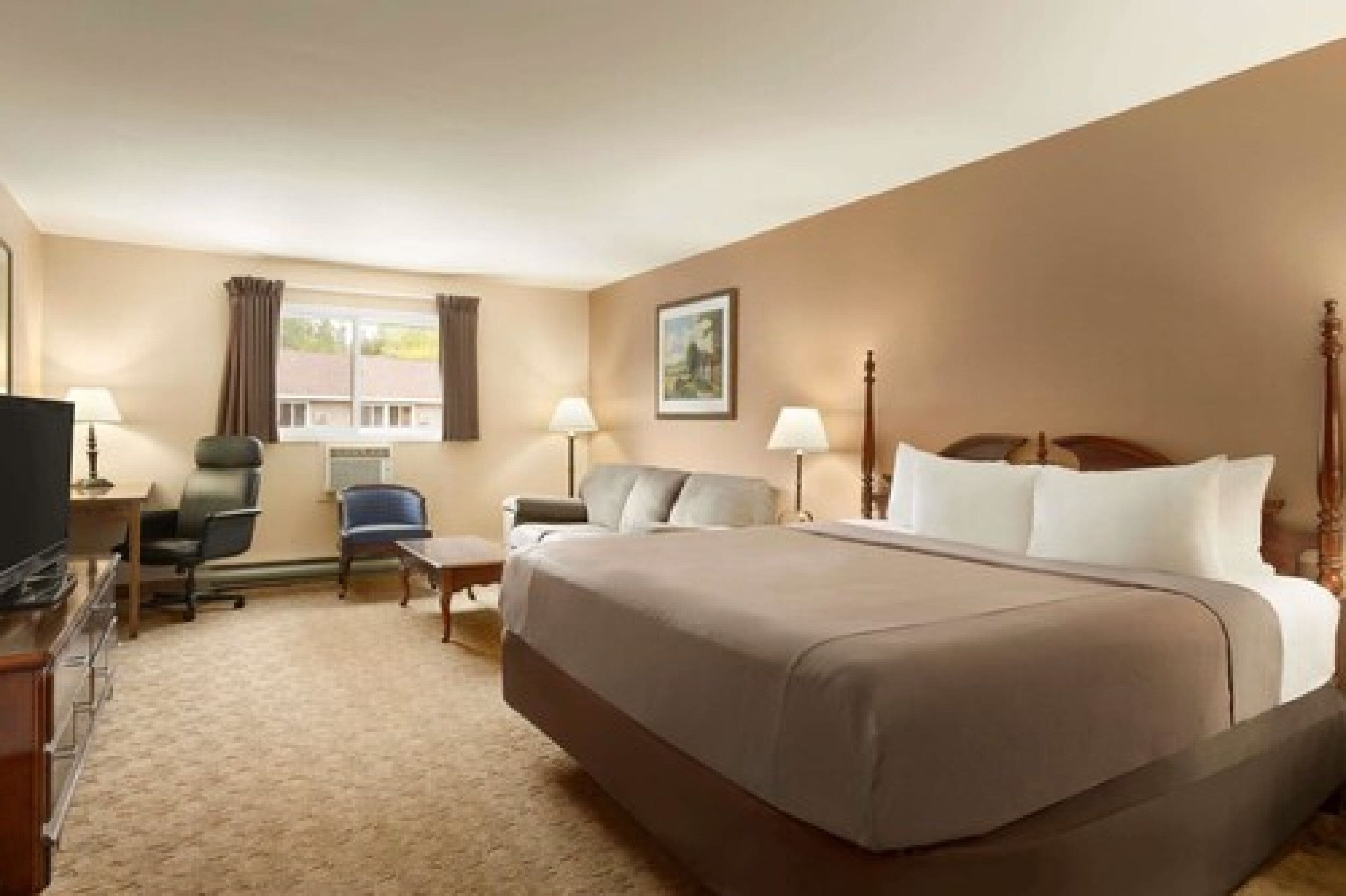 A hotel room with a large bed, a desk, a chair, and a television.