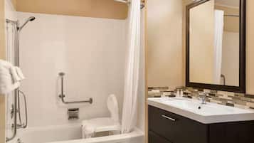 Een badkamer met een wit bad, een douche met glazen deur, een wastafel en een spiegel.