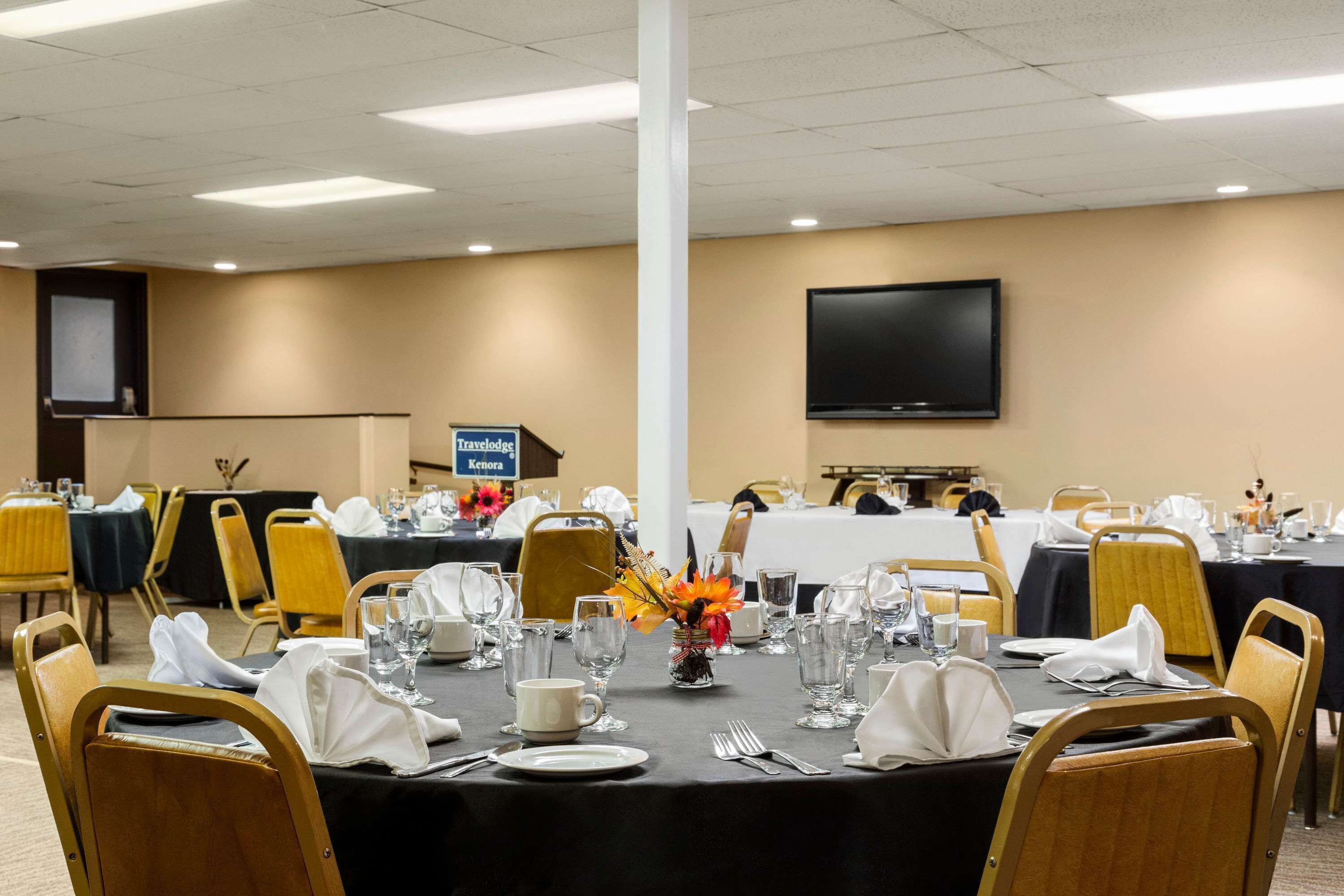 Une salle de conférence avec des tables disposées pour une réunion, équipée de porte-noms, de verres à eau et d’une enseigne indiquant « Travelodge ».