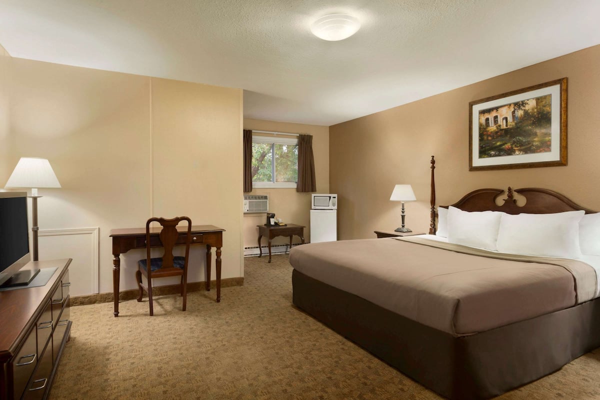 A hotel room with a bed, desk, chair, television, and a painting on the wall.