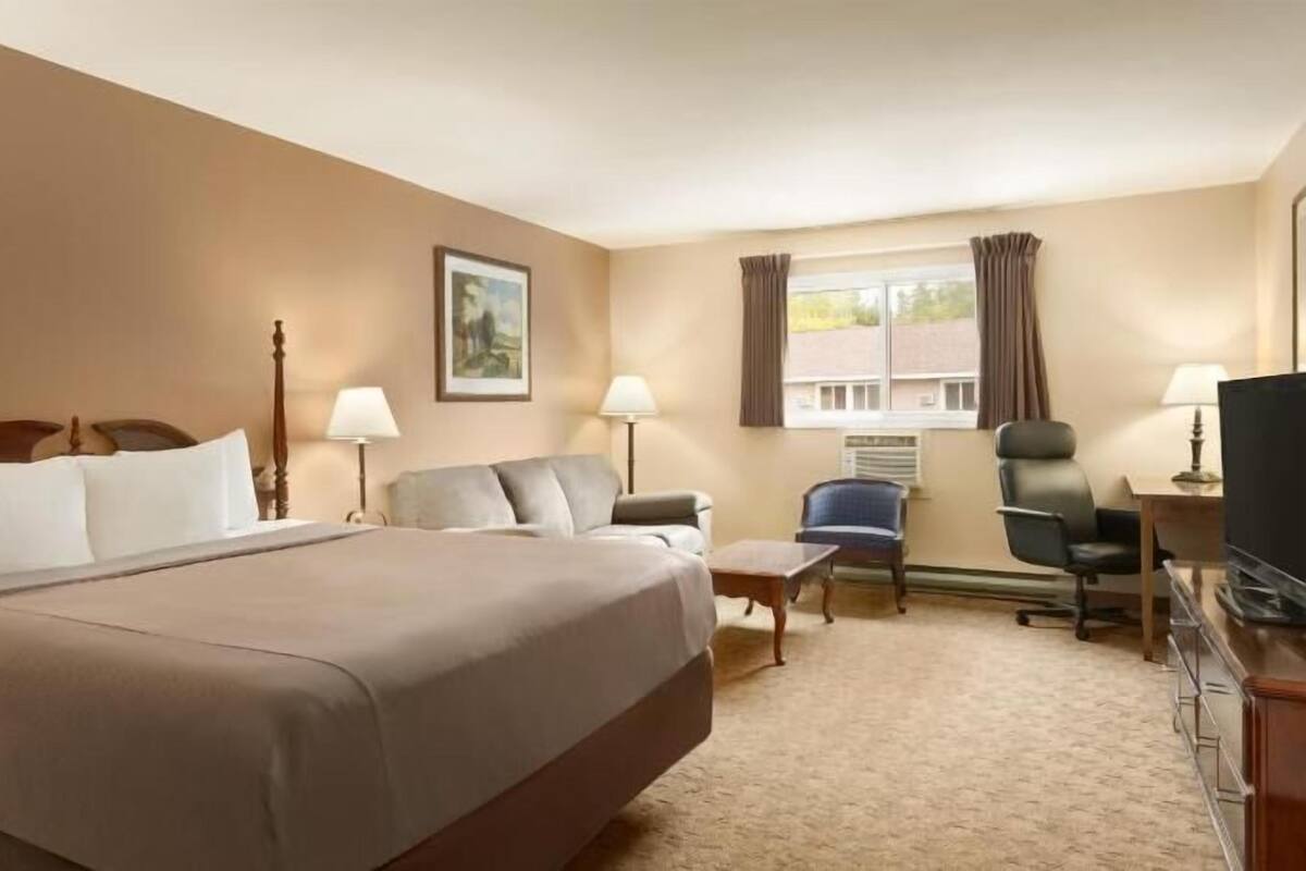 A hotel room with a large bed, a sofa, a desk with a chair, a television, and a window with curtains.