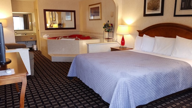 Ein Hotelzimmer mit einem großen Bett, einem Schreibtisch, einem Schminktisch mit Spiegel, einer roten Lampe und gerahmten Bildern an der Wand.