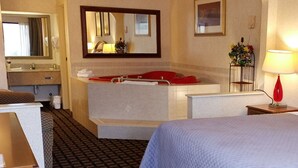 Ein Hotelzimmer mit einem großen Bett, einer separaten Sitzecke, einer Badewanne, einem Spiegel und einem Nachttisch mit Lampe.
