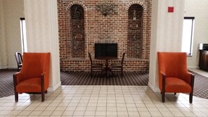 Eine Lobby mit einem Kamin aus Ziegelsteinen, zwei orangefarbenen Sesseln und einem Fliesenboden.