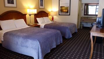 A hotel room with two beds, a desk, a television, and a bathroom visible through an open door.