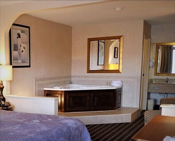 A hotel room with a large bed, a separate bathroom with a bathtub, a vanity with a mirror, and a framed picture on the wall.
