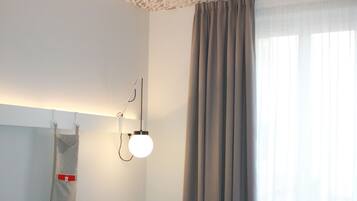 Une chambre d’hôtel avec un lit, un bureau, une chaise, un téléphone, une poubelle rouge et une fenêtre avec des rideaux.