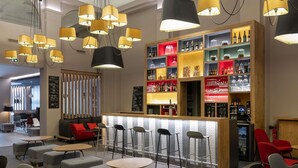 A modern bar area with multiple seating options, including bar stools and round tables, and a variety of bottles and glasses on shelves. - ibis Lyon Centre Perrache (Lyon)