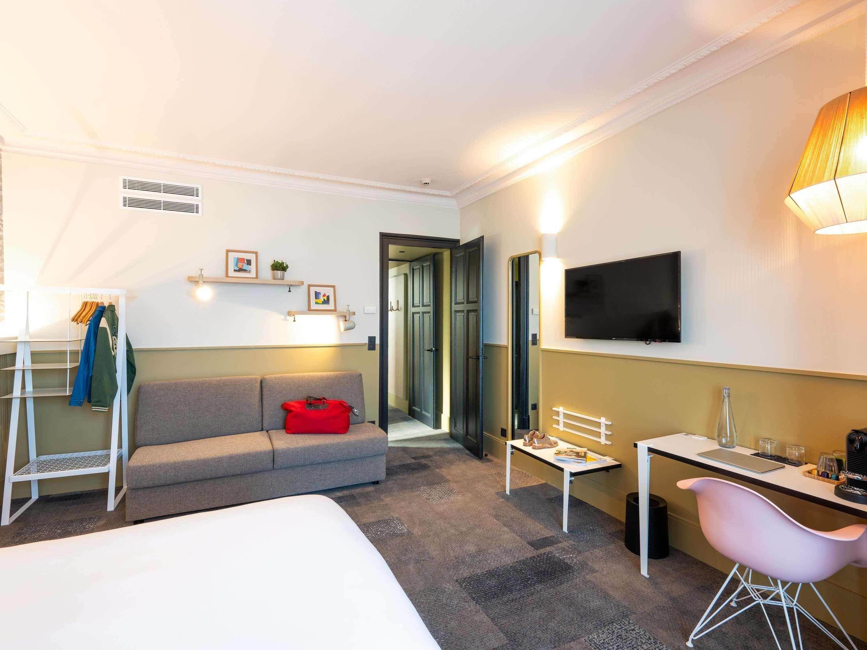 A hotel room with a bed, a desk, a chair, a TV, and a sofa.
