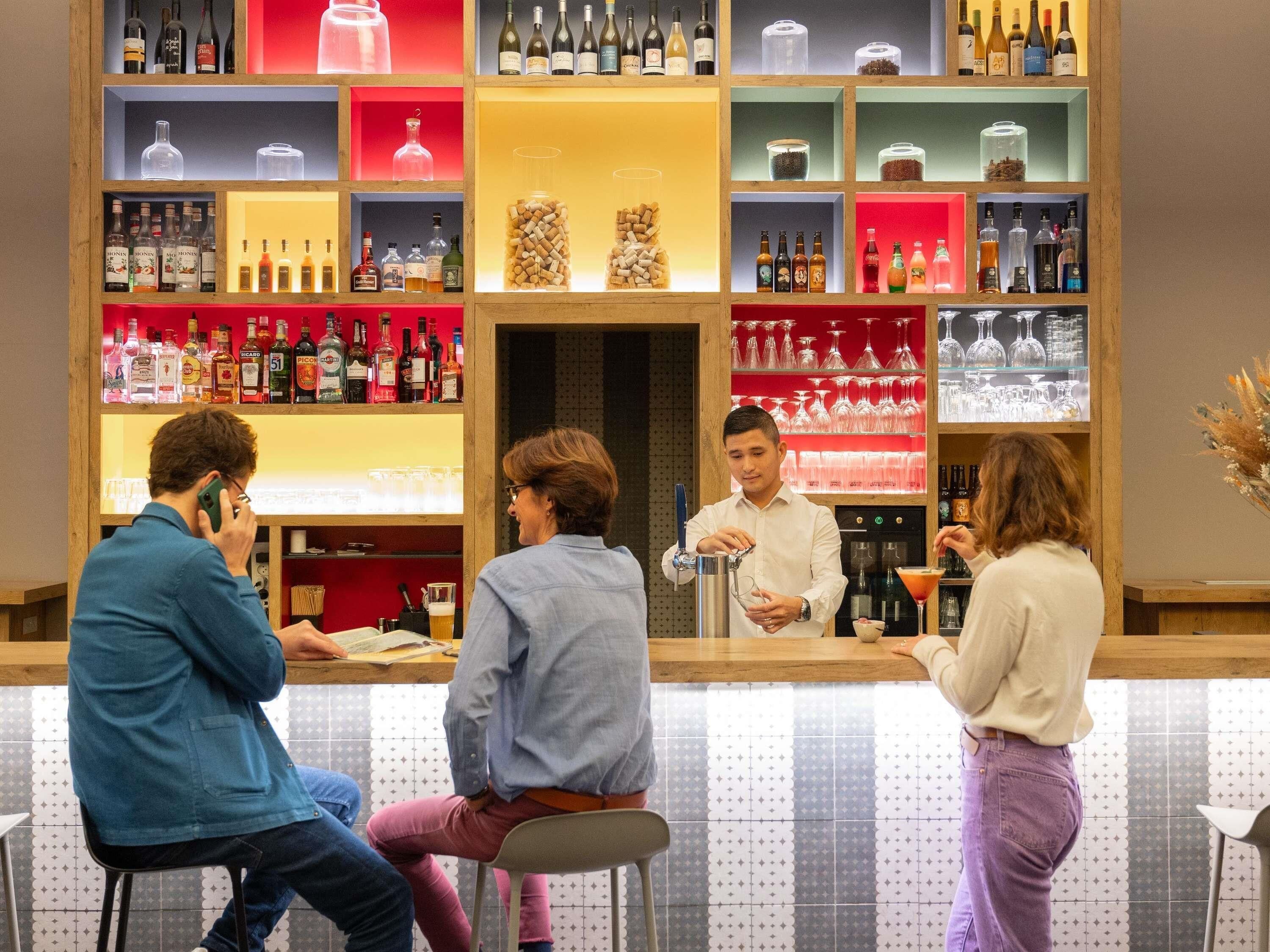 Uma área de bar com várias prateleiras de garrafas e copos, um balcão e banquetas.