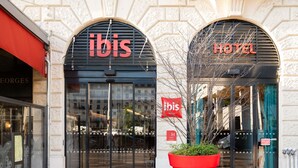 A hotel entrance with 'ibis' signage, a large red planter, and a 'HOTEL' sign above the door. - ibis Lyon Centre Perrache (Lyon)