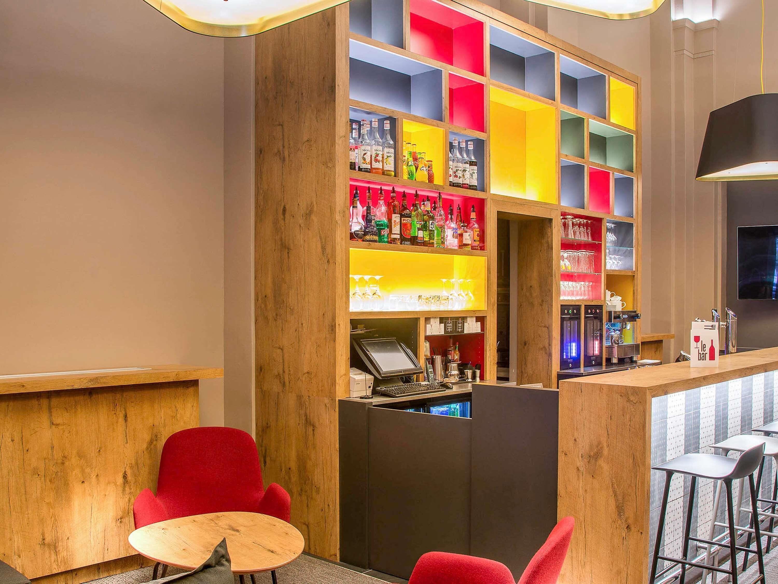 A bar area with a wooden counter, red chairs, and a colorful shelving unit with bottles.