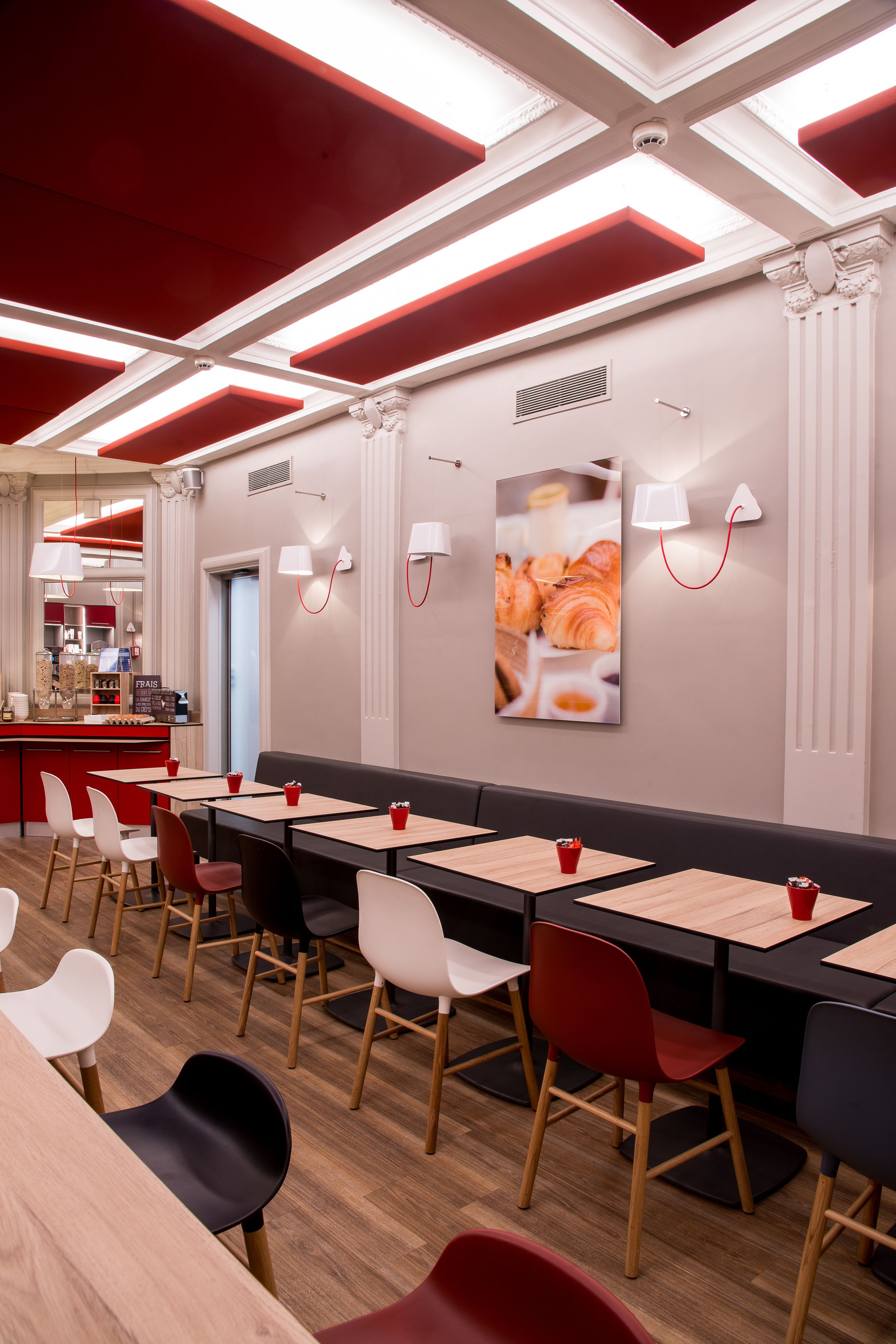 A modern restaurant interior with wooden tables, red and black chairs, and a red ceiling design.