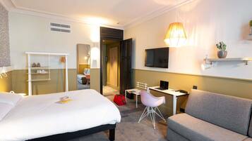 Habitación de hotel con cama, escritorio, silla, sofá, televisor y espejo.