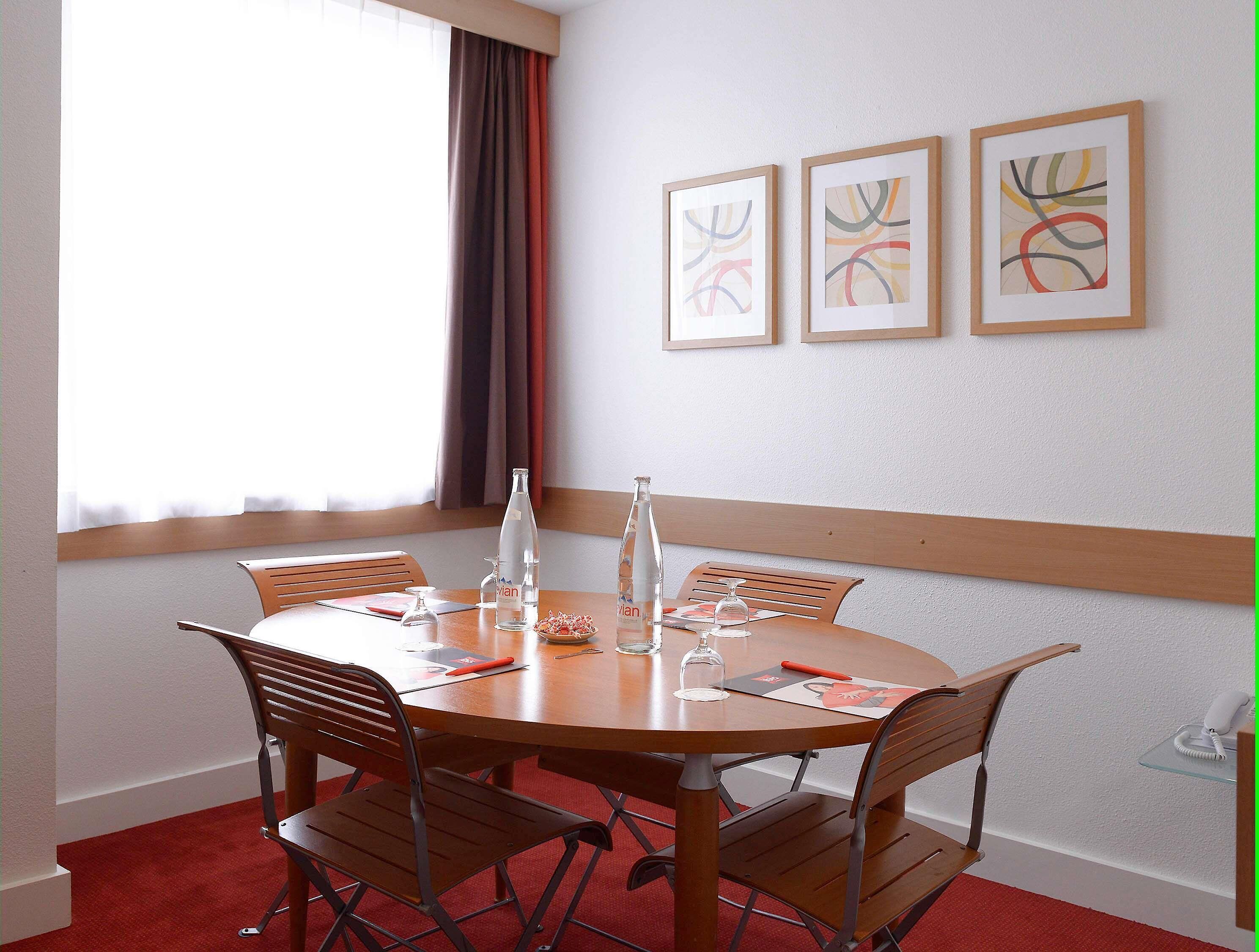A round table with six chairs, a bottle, and a glass on it. There are three framed artworks on the wall.