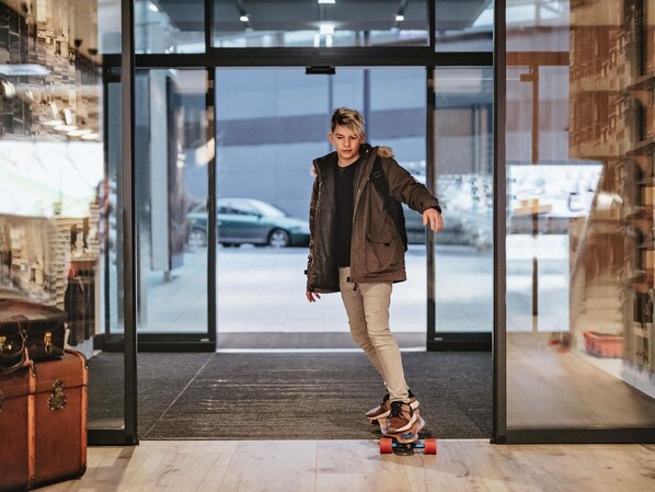 A person skateboarding inside a building with a glass door leading to the outside.