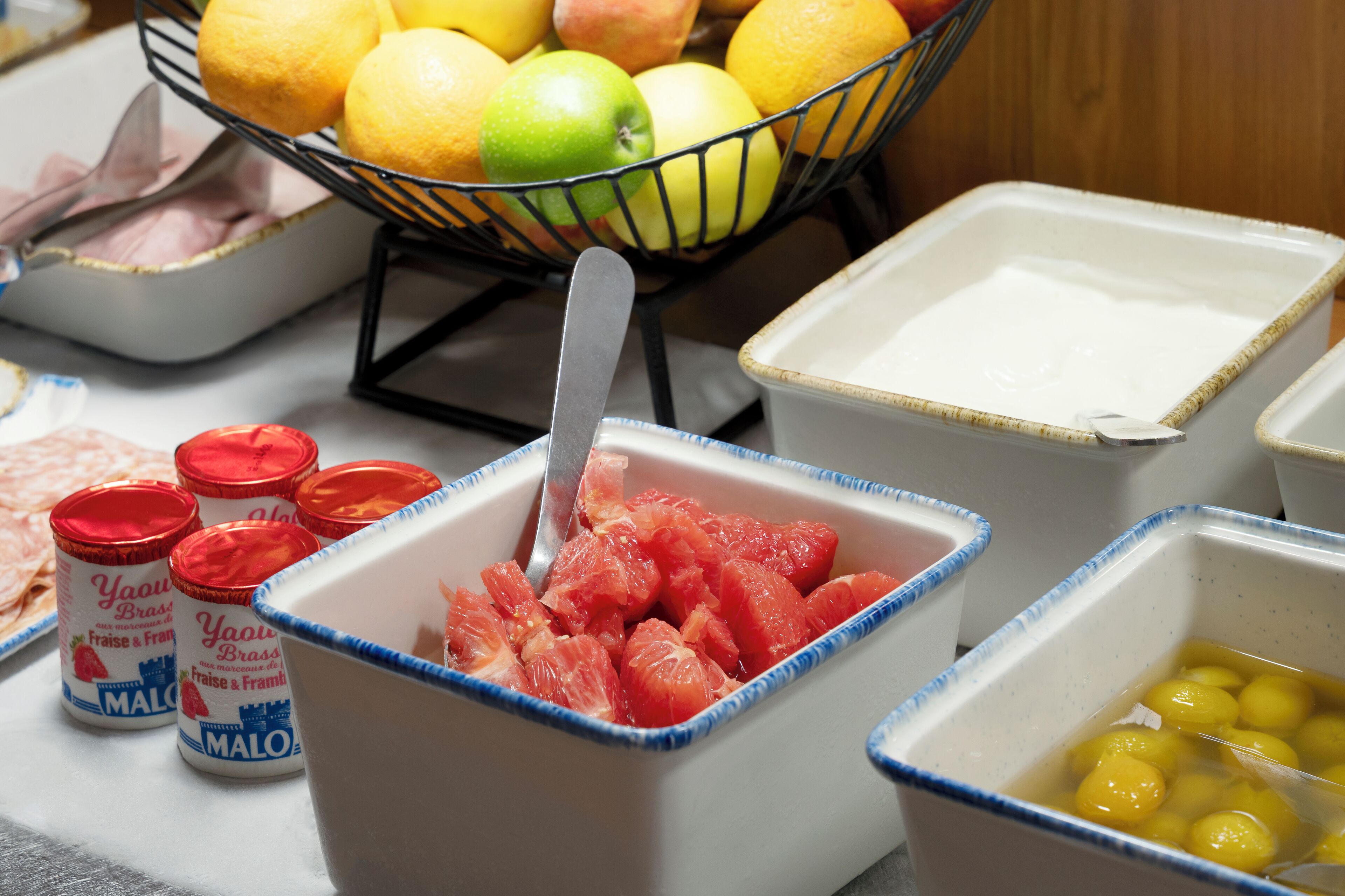 A table with various food items including a bowl of grapefruit, a bowl of yellow fruit, and containers of yogurt.