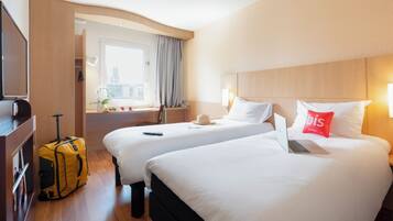 Habitación de hotel con dos camas, una maleta, una computadora portátil y una ventana con vistas a edificios.