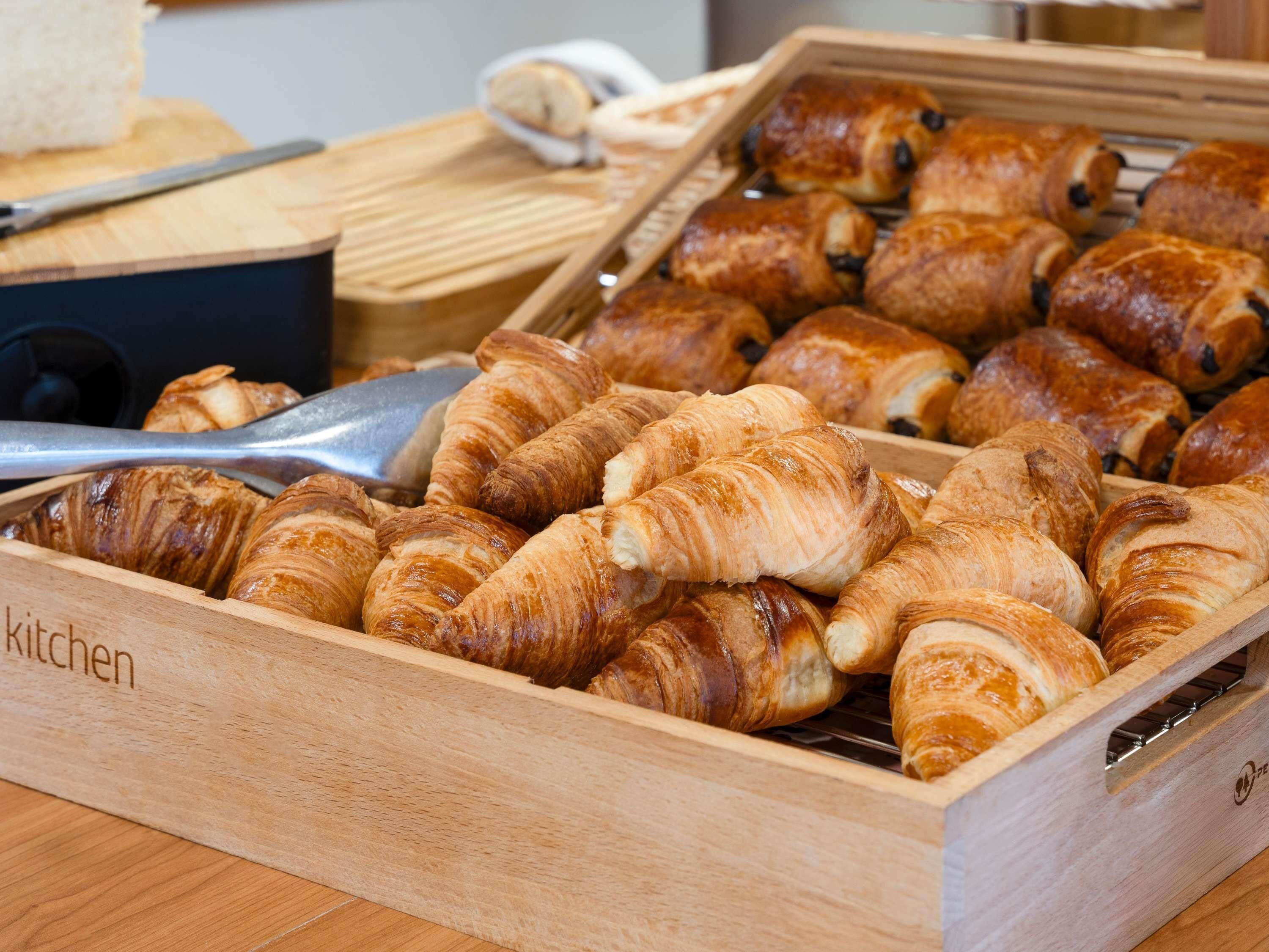 A wooden box filled with assorted pastries, including croissants and chocolate-filled pastries.