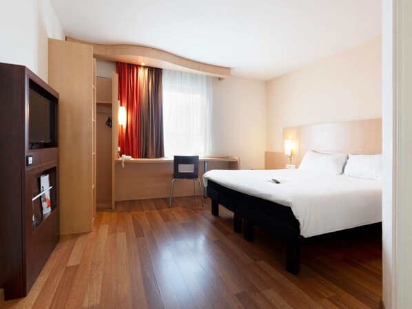 Habitación de hotel con cama, escritorio, silla, televisión y ventana con cortinas.