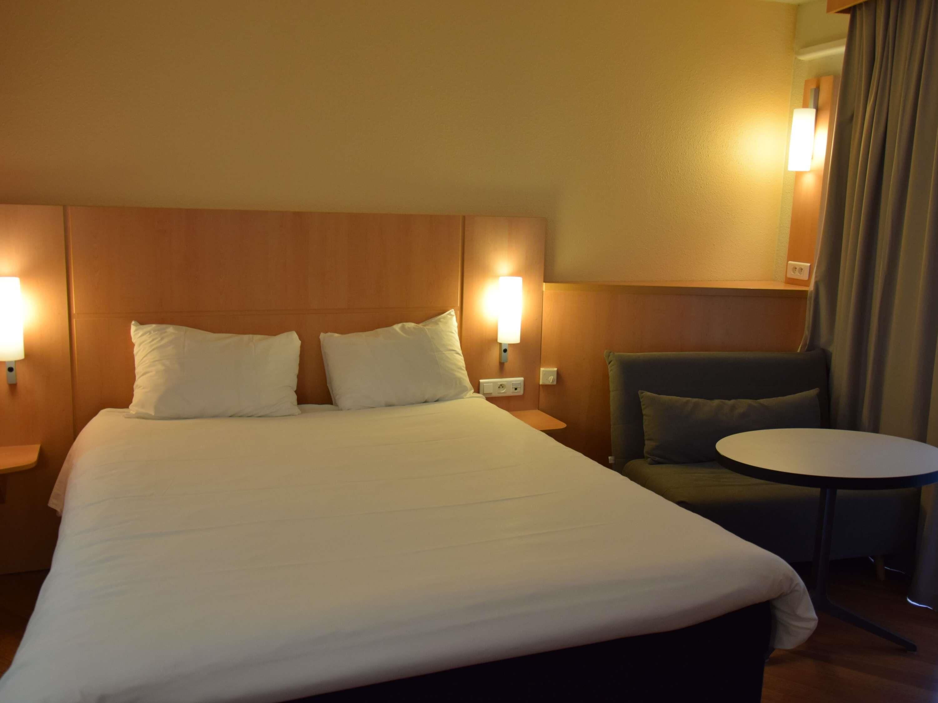 Habitación de hotel con una cama grande, dos lámparas de noche, una mesita redonda y una silla.