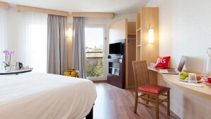 A hotel room with a bed, a desk with a laptop, a chair, a TV, and a balcony with curtains. - ibis Nancy Centre Gare et Congres (Nancy)