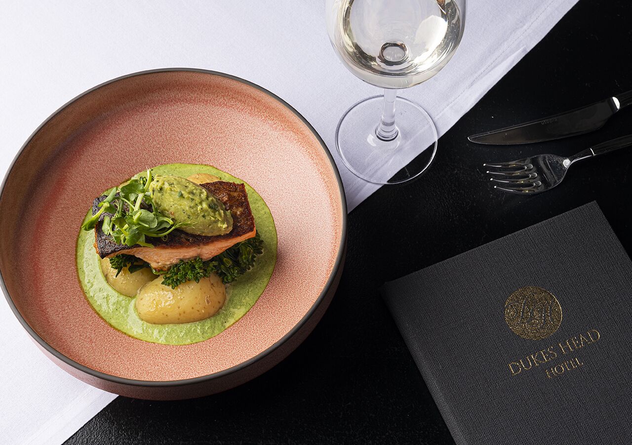 A plate of food with a glass of white wine and a black menu on a table.