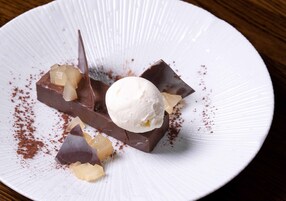 Un postre en un plato blanco con base de chocolate, una bola de helado y trozos de fruta.