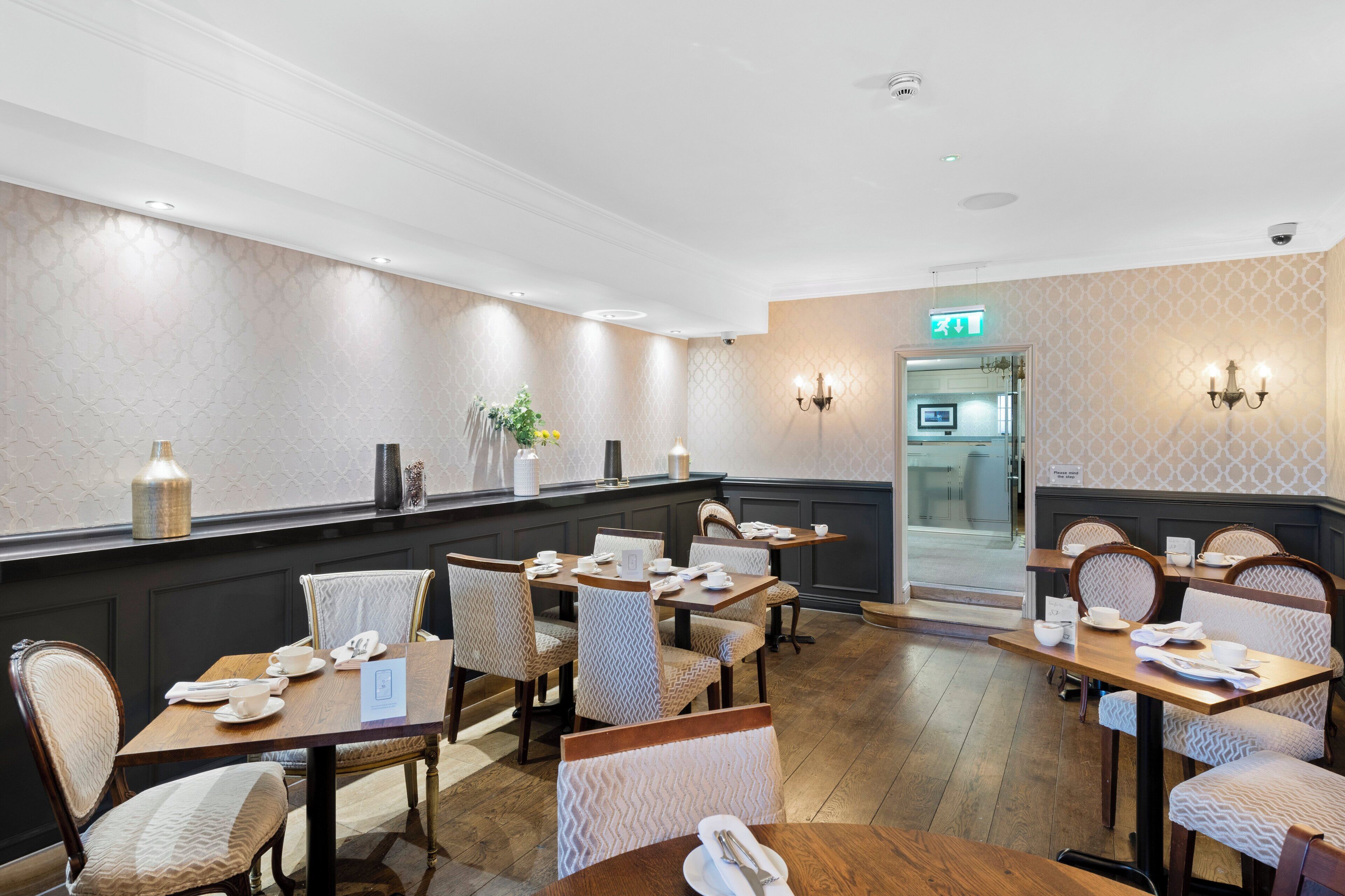 A hotel dining area with multiple tables and chairs, a reception desk, and a patterned wall.
