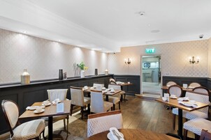 Un comedor de hotel con varias mesas y sillas, una recepción y un muro decorado.