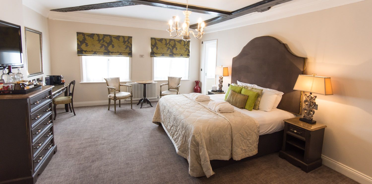 A bedroom with a large bed, a desk, and a chair. There is a dresser and a lamp on the side.