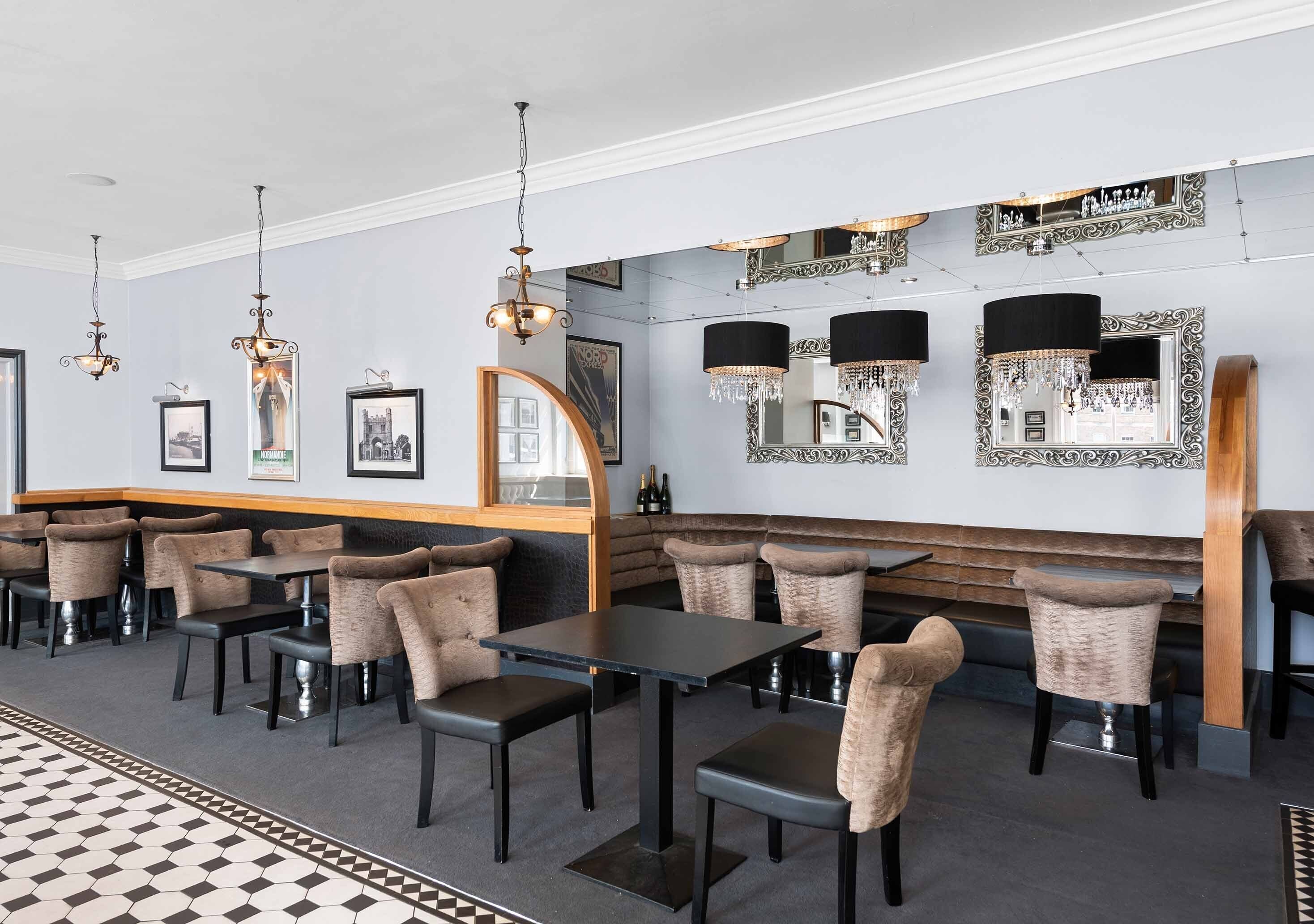 A restaurant with a long counter, cushioned chairs, and hanging chandeliers.