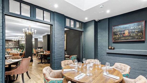Un comedor con una mesa redonda de madera dispuesta para seis personas, rodeada de sillas tapizadas con un estampado colorido.