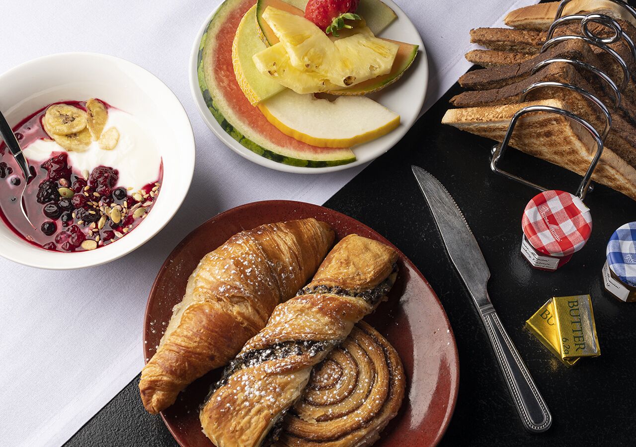 A breakfast setting with croissants, sliced fruits, and a bowl of yogurt with berries.