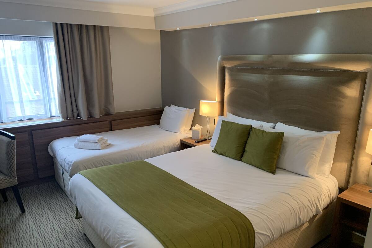 Ein Hotelzimmer mit zwei Betten, einem Schreibtisch und einem Fenster mit Vorhängen.