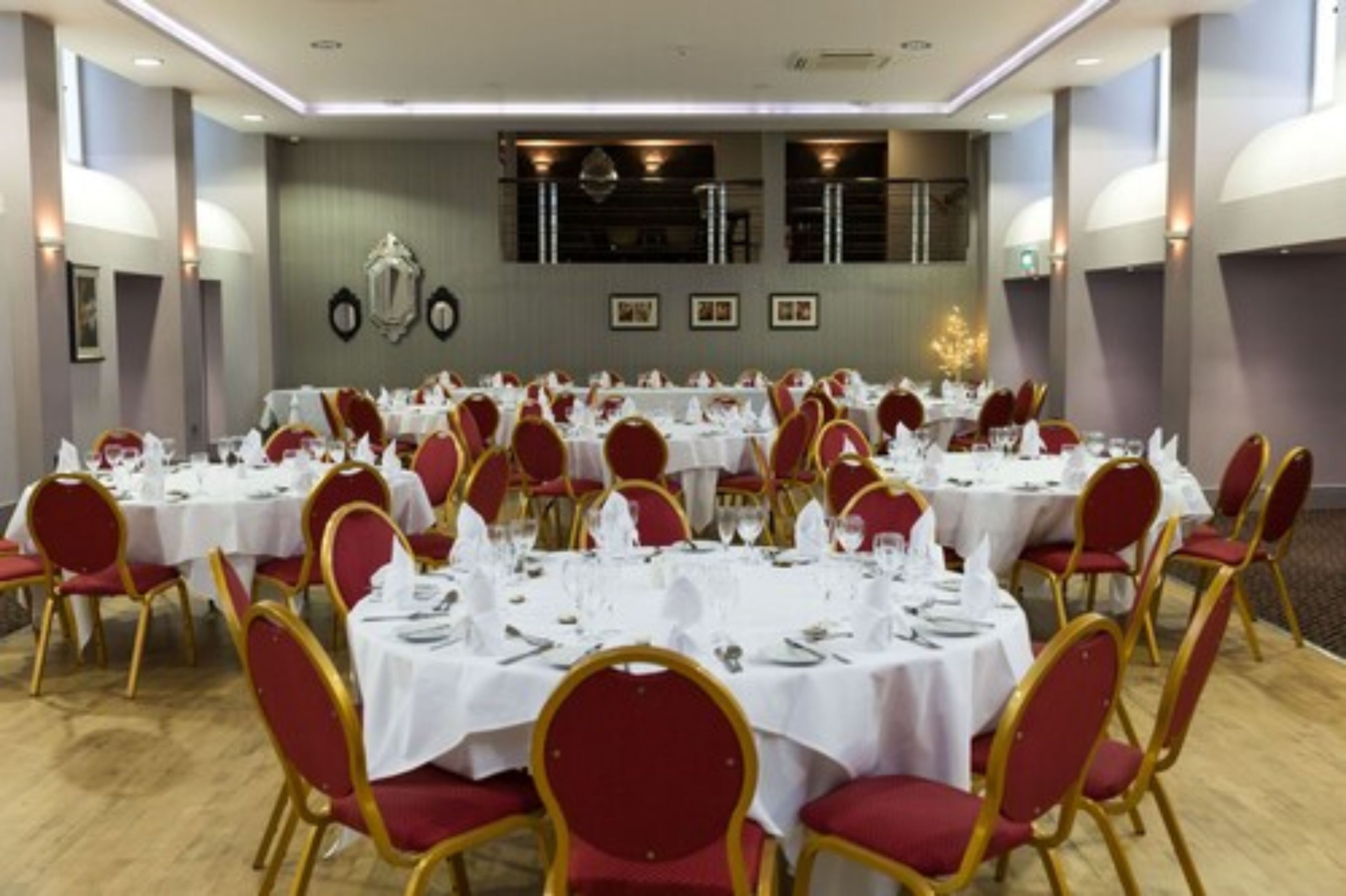 Un salón de banquetes con mesas redondas dispuestas para comer, sillas tapizadas en rojo y una araña de cristal.