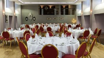 A banquet hall with round tables set for dining, red upholstered chairs, and a chandelier.