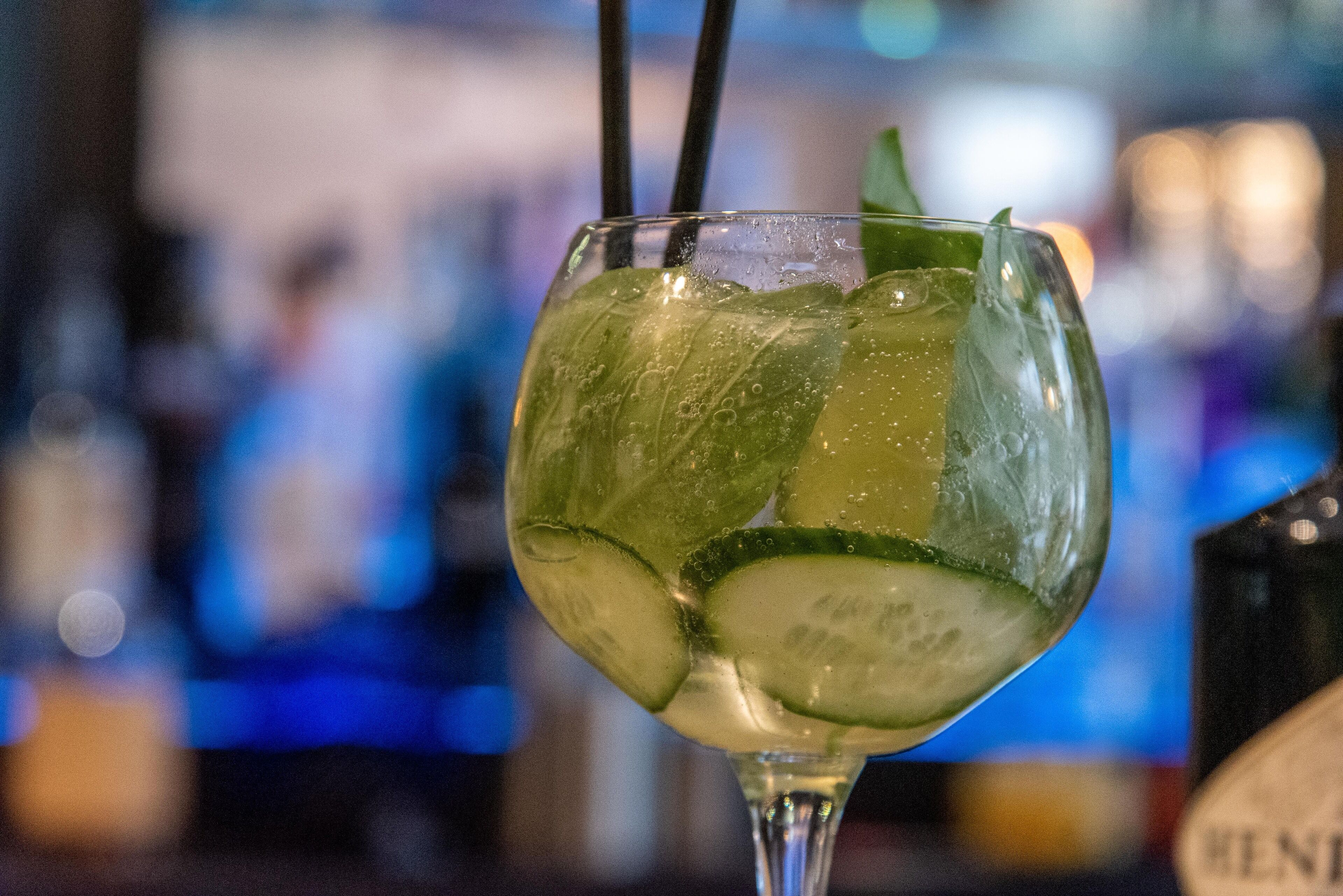 Un vaso de cóctel con hielo y rodajas de lima, con un fondo desenfocado que sugiere un bar.