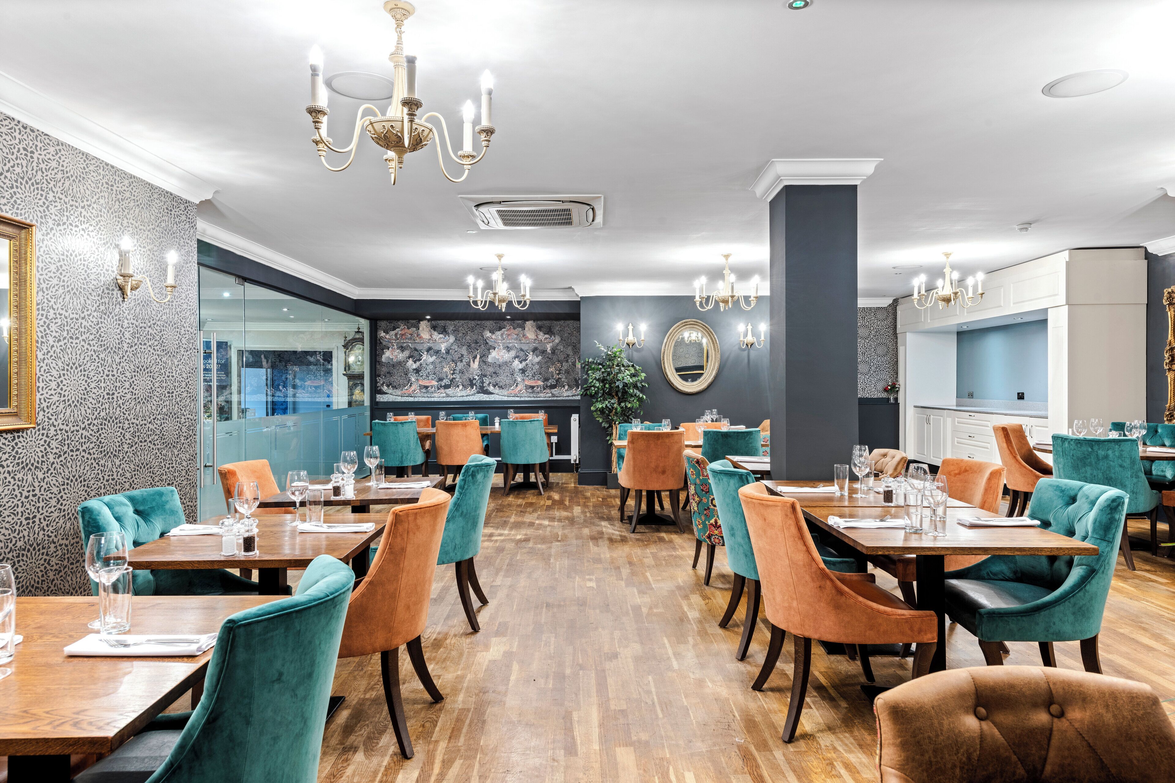 A restaurant with wooden tables and teal chairs, chandeliers, and a patterned wall.