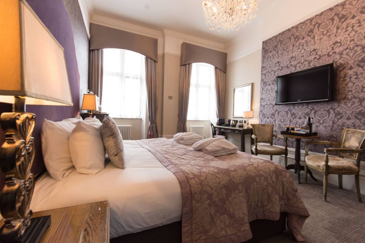Ein Hotelzimmer mit einem großen Bett, einem Schreibtisch, einem Sessel, einem Fernseher und einer Chandelier.