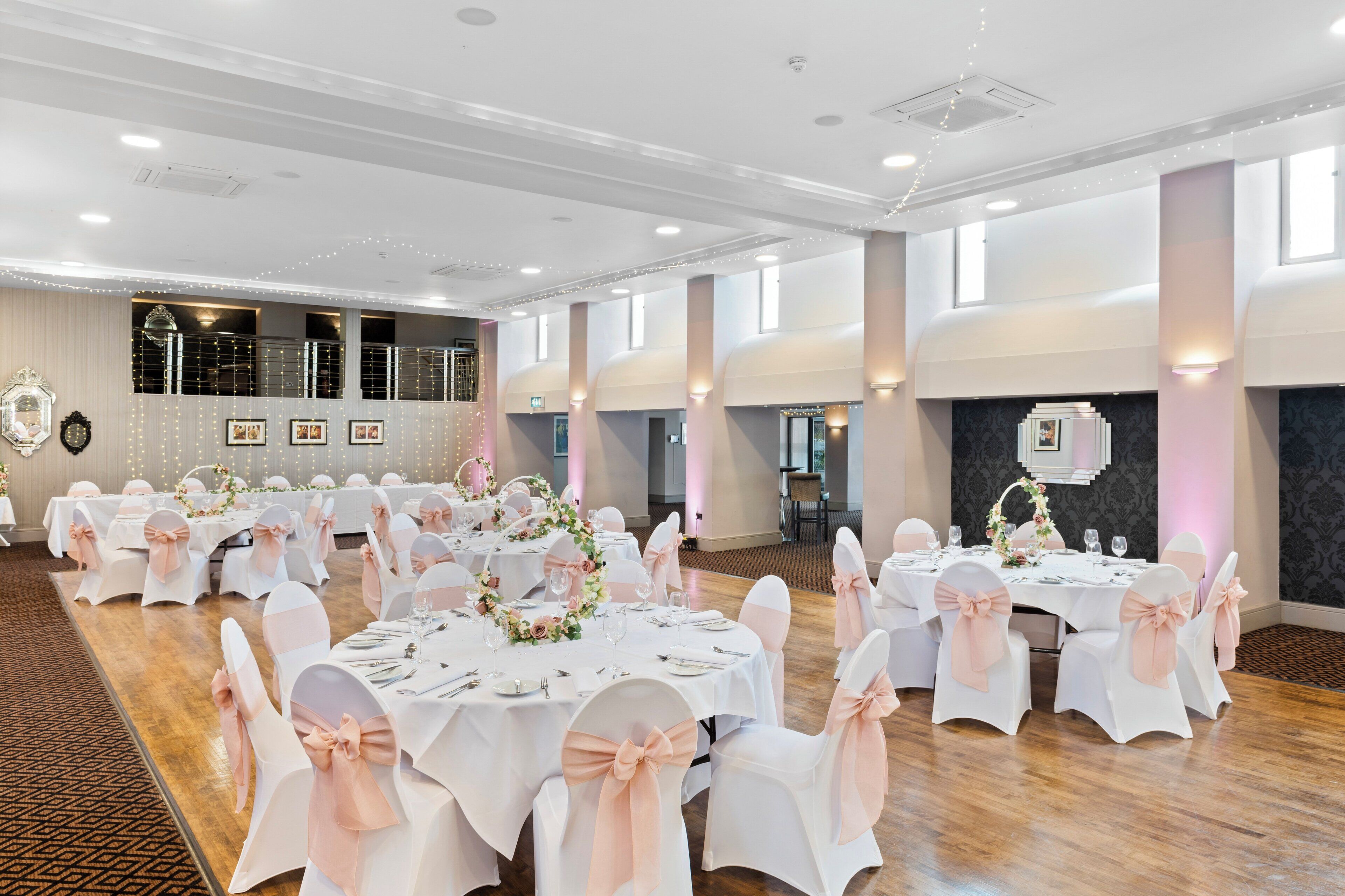 A banquet hall with round tables, white tablecloths, and chairs with pink sashes.