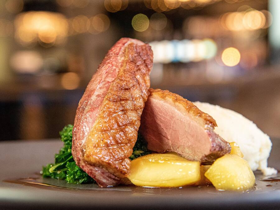 A dish with meat, potatoes, and greens on a plate.