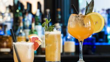 Three cocktails on a bar counter with a blurred background of bottles.
