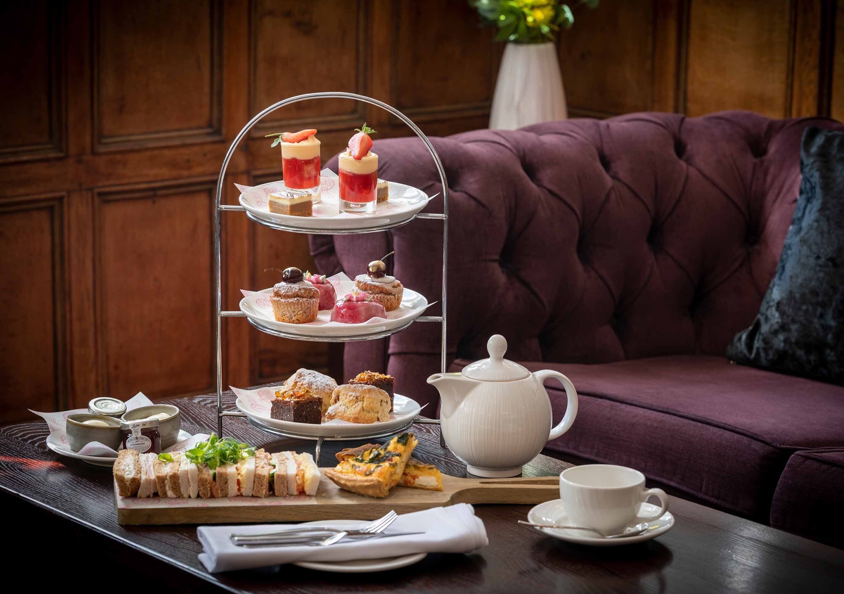 A three-tiered dessert tray with various pastries and a teapot on a table.